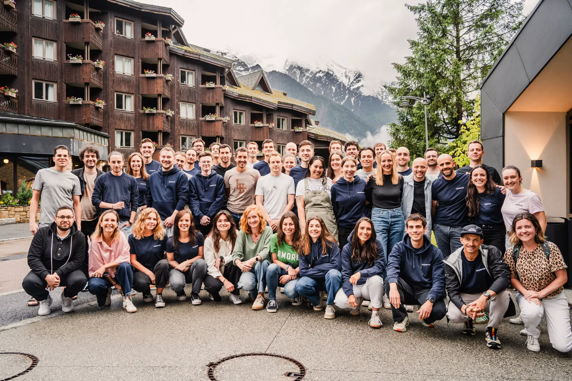 The Campus Coach team at the Chamonix retreat in June 2025, about fifty people in front of a chalet, the snowy massif behind.