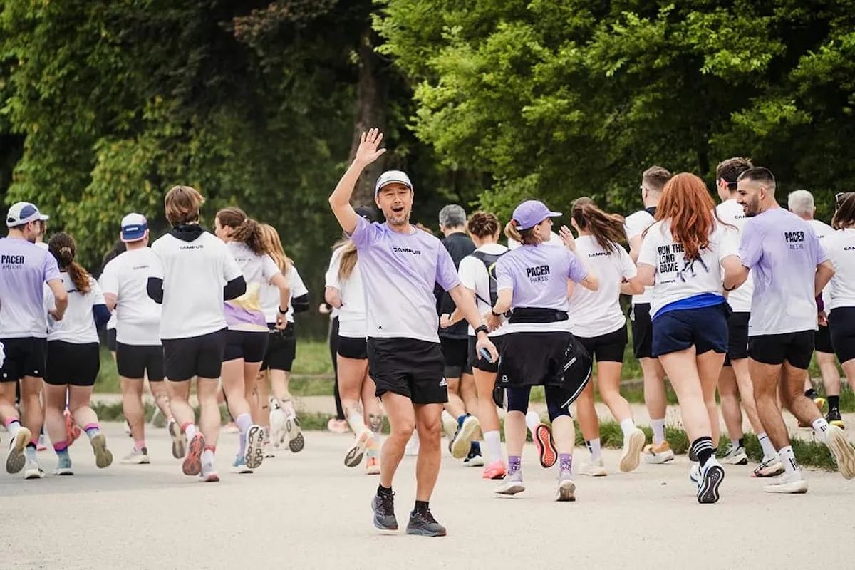 A group run in a park, seen from behind: about thirty runners in purple and white Campus tee-shirts, marked Pacer Paris and Pacer Amiens. In the center, facing the camera, a man raises his hand.